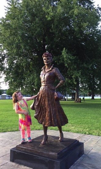 A little girl standing next to a statue of a woman.