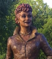 A statue of lucille ball in front of trees.