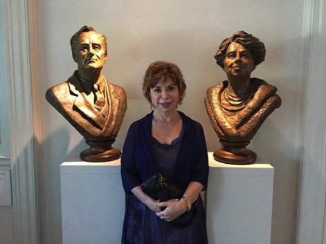 A woman standing between two busts of people.