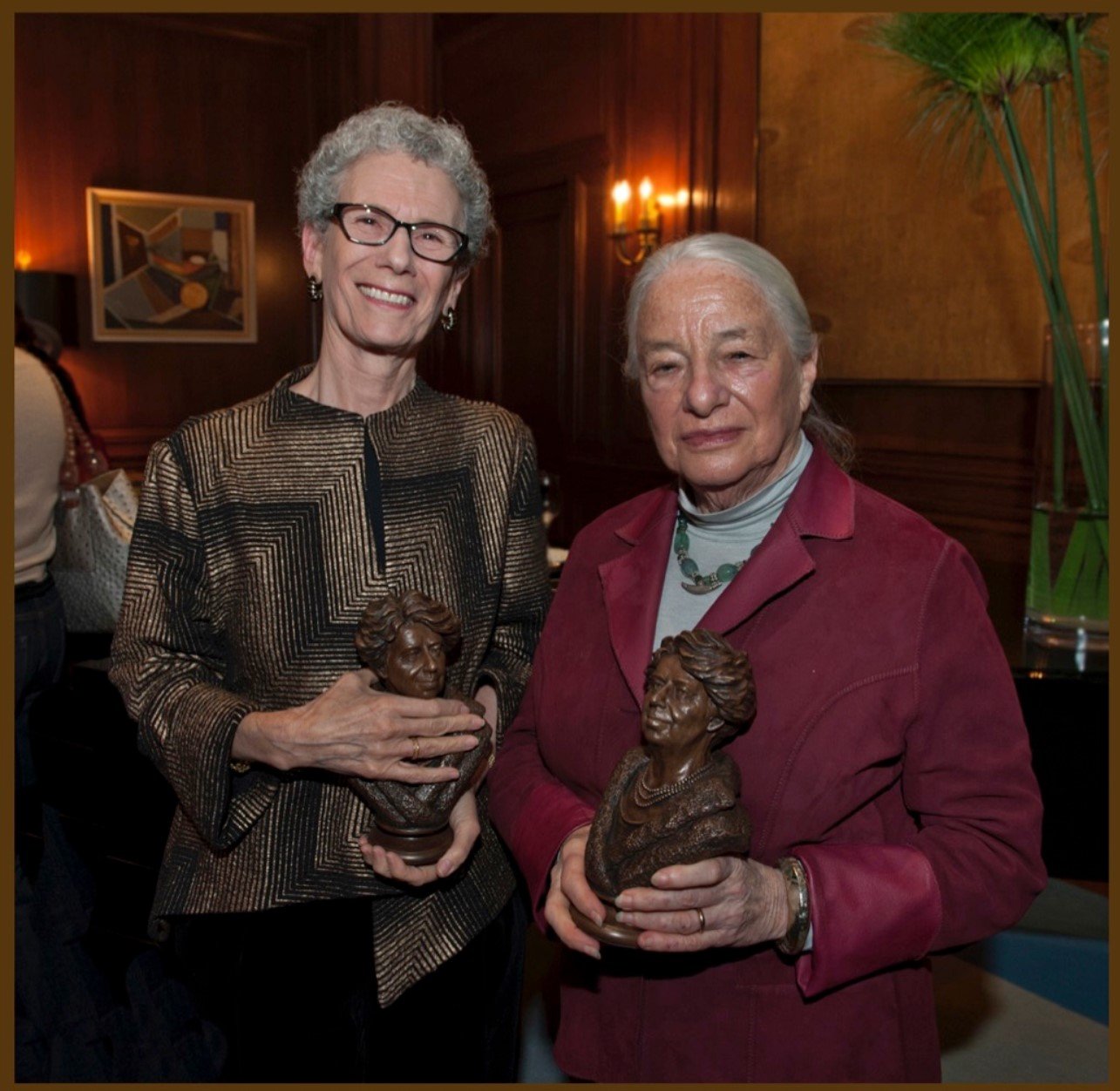 Two women holding up small statues of rabbits.
